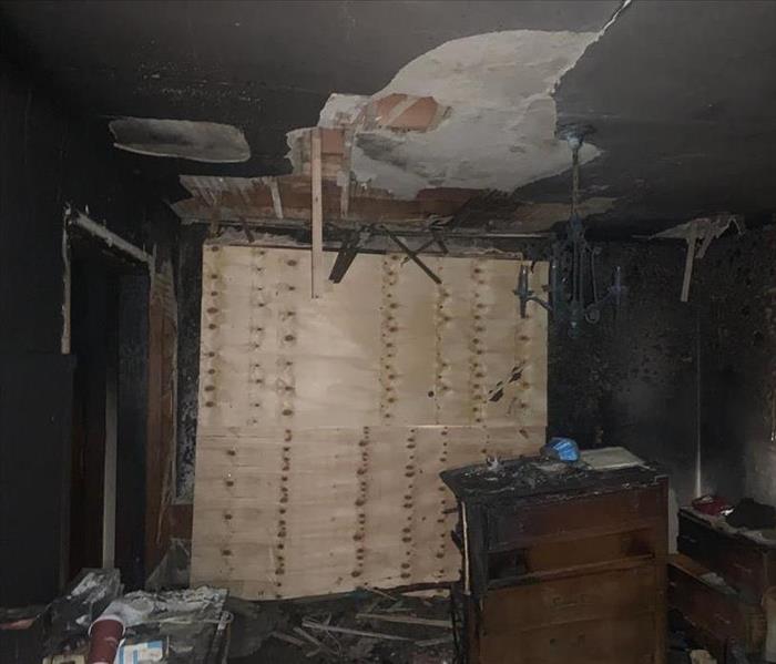 Burnt dressers and damaged ceiling in room with boarded windows